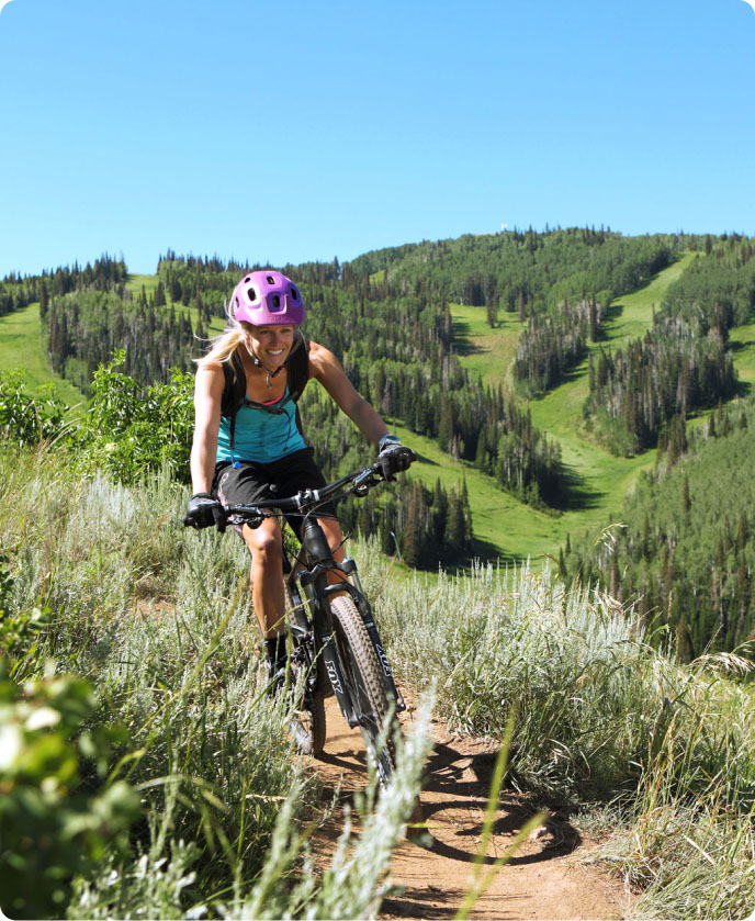 Girl on a bike with a purple helmet and blue shirt mountain biking down at park city