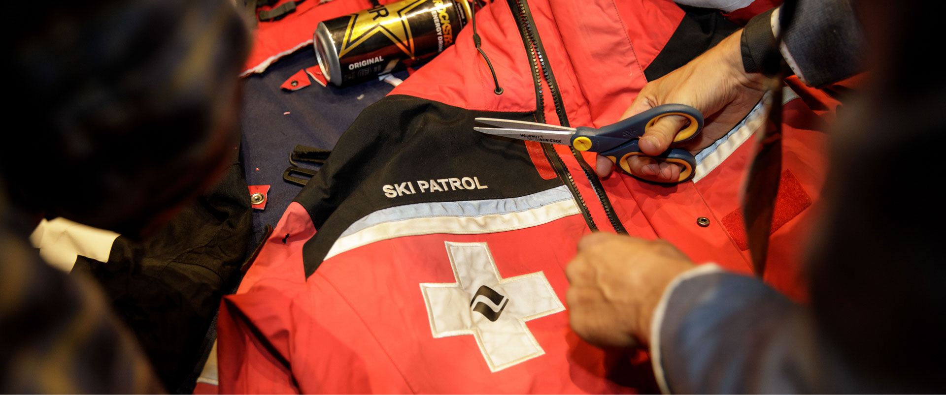 Hand holding scissors over an old ski patrol jacket