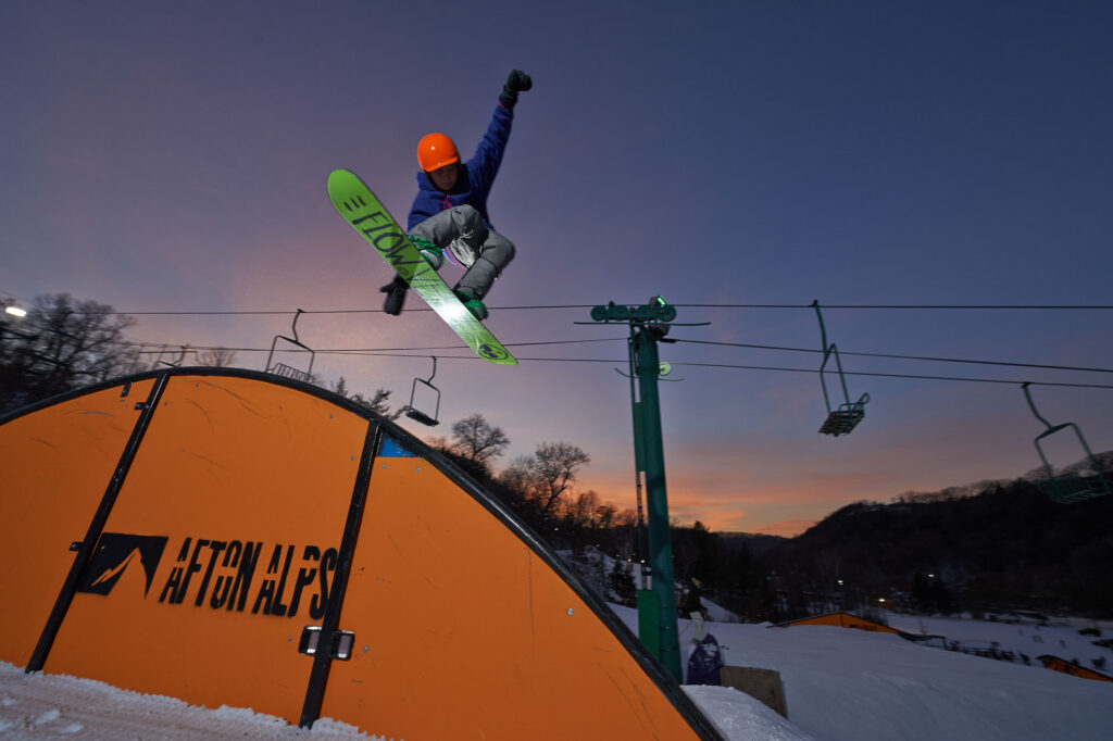 Snowboarder in a terrain park going off of a jump with hand in their air