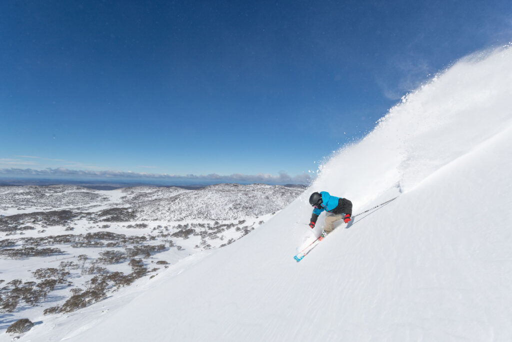 Image of skier in a blue jacket going down a powder run in Australia