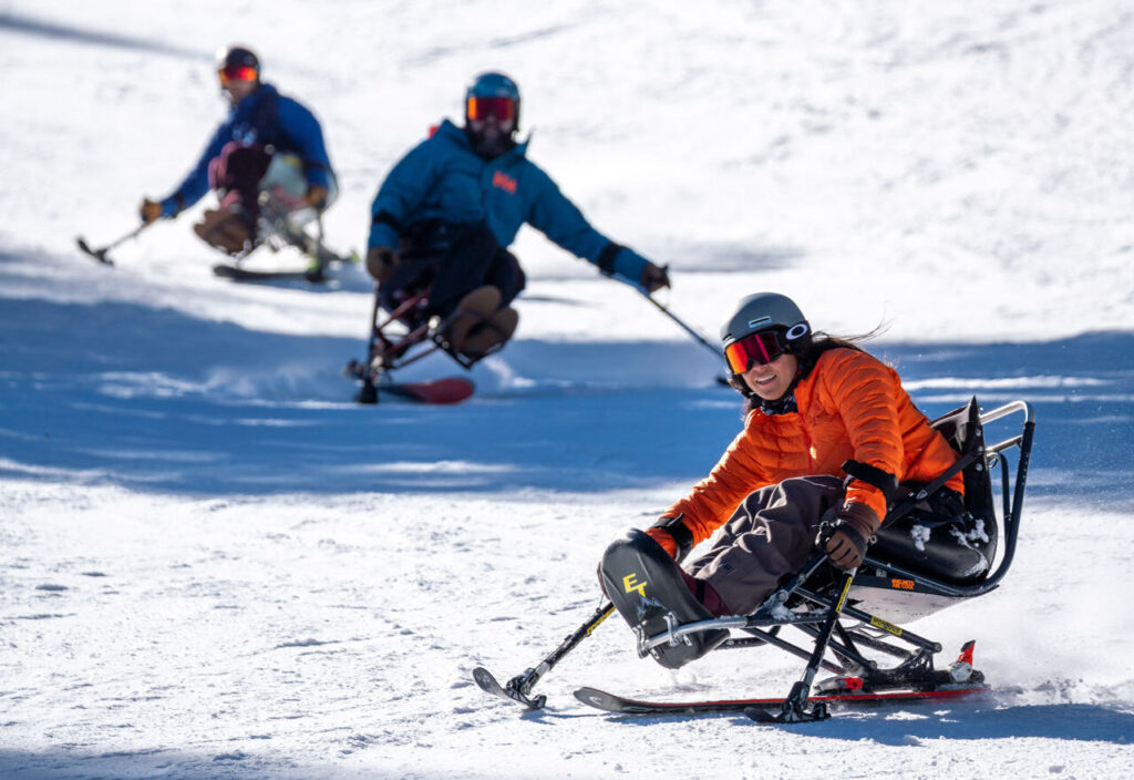 Group of 3 sit skiers going down a run together