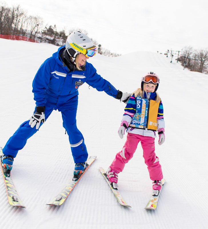 Ski instructor in a blue jacket helping a young student in a ski lesson