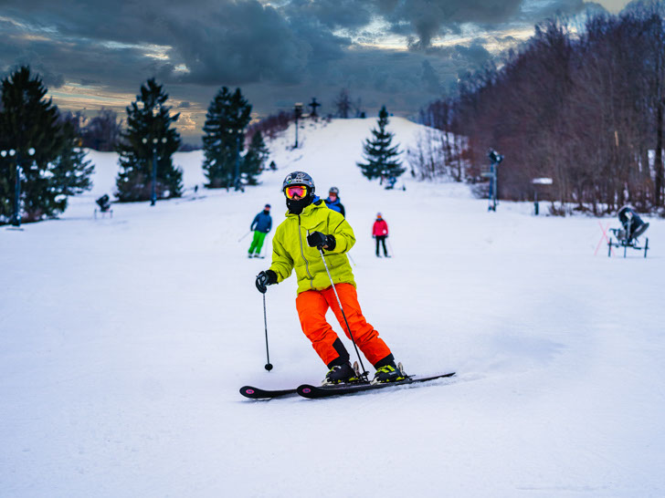 Skier in a bright yellow jacket with friends in the background skiing down a run at alpine valley