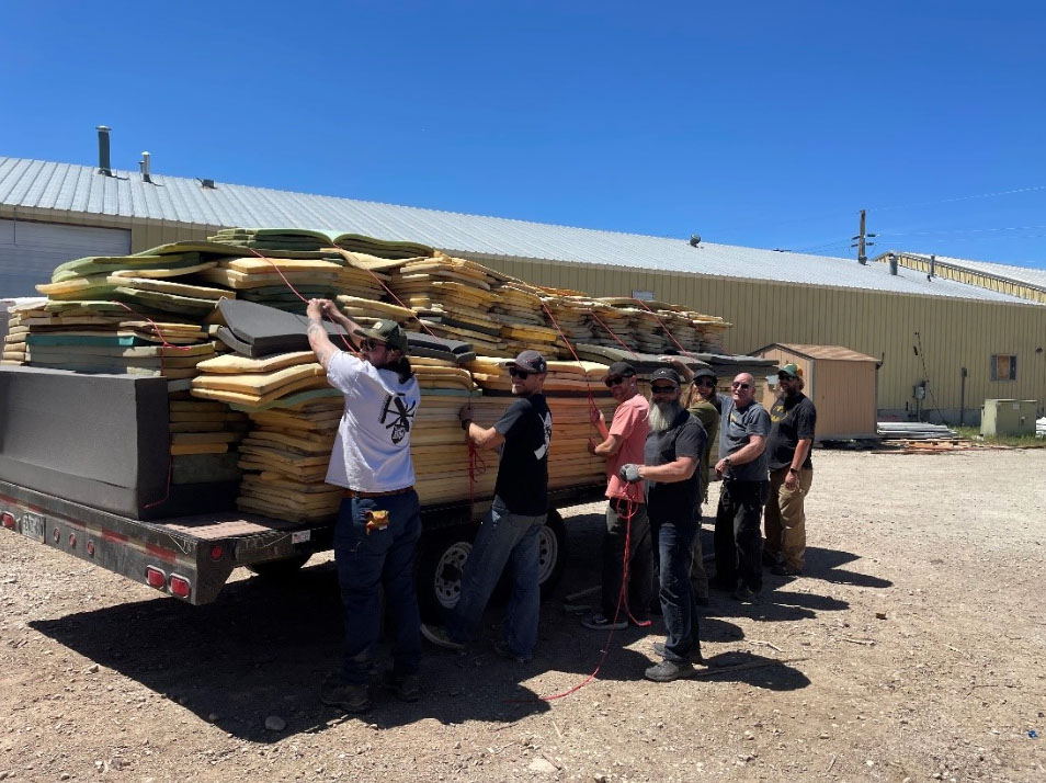 A group of 7 men smiling strapping use foam pads from chairlifts on a trailer