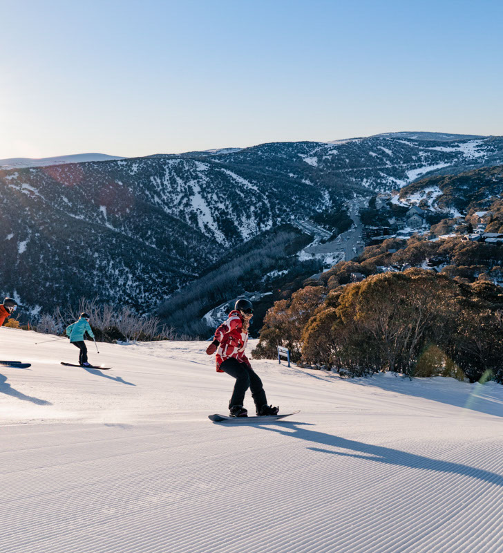Group of skiers and a snowboard going down a groomed run at Falls Creek