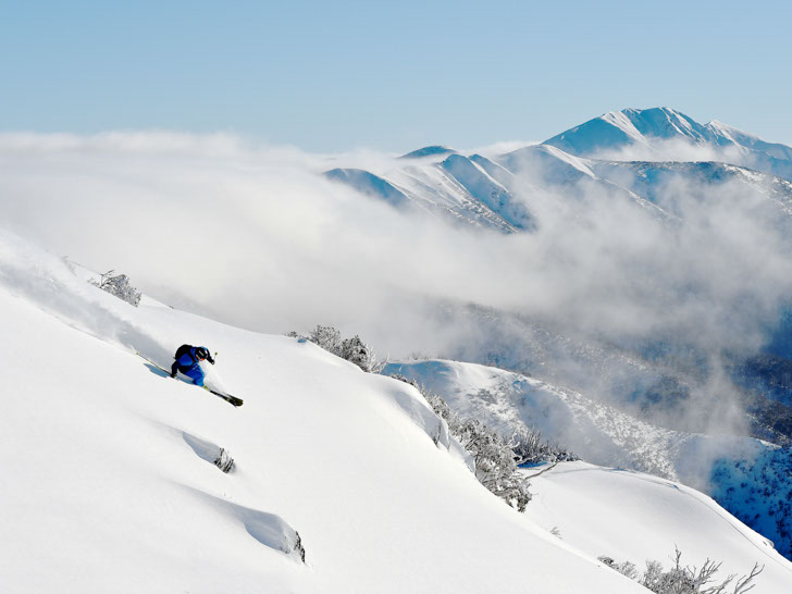 Skier in a blue outfit taking a wide turn on a powder run at Hotham