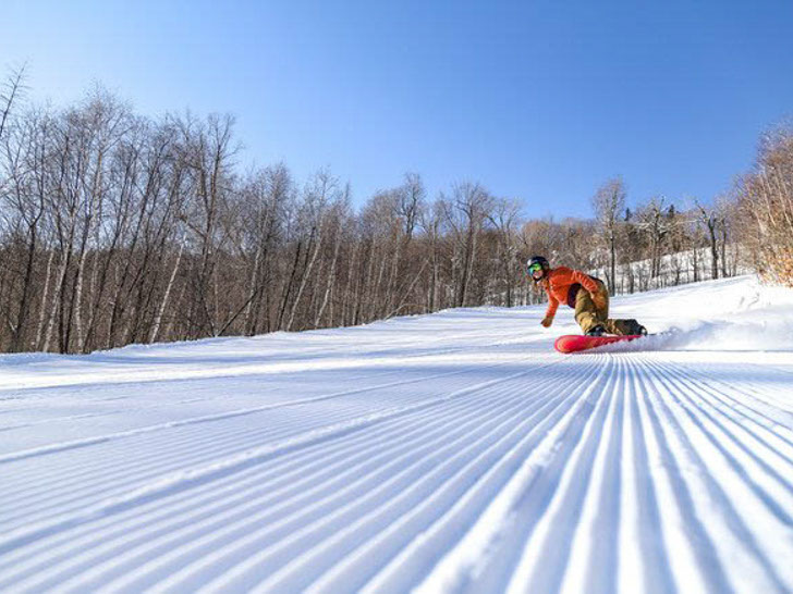 Snowboarder in red jacket carving down a groomed run