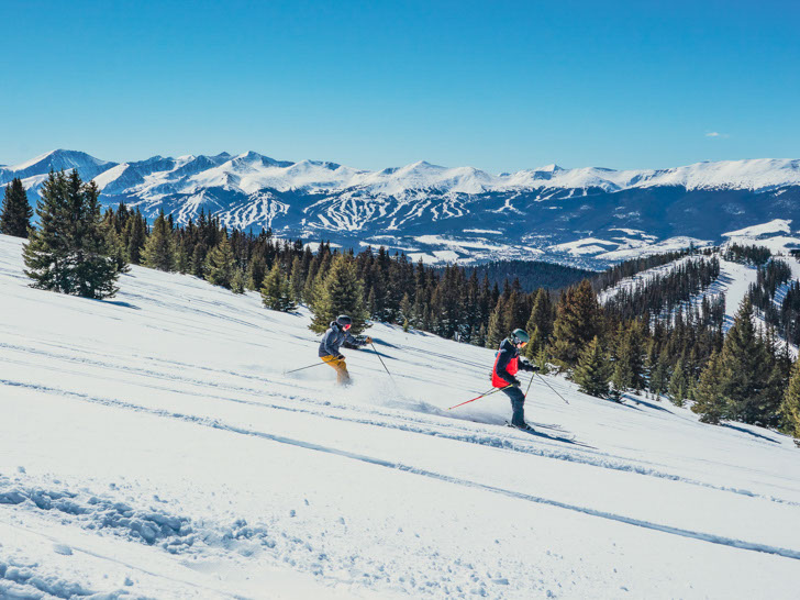 Two skiers going down a run at Keystone's Bergman Bowl with Breckenridge in the background