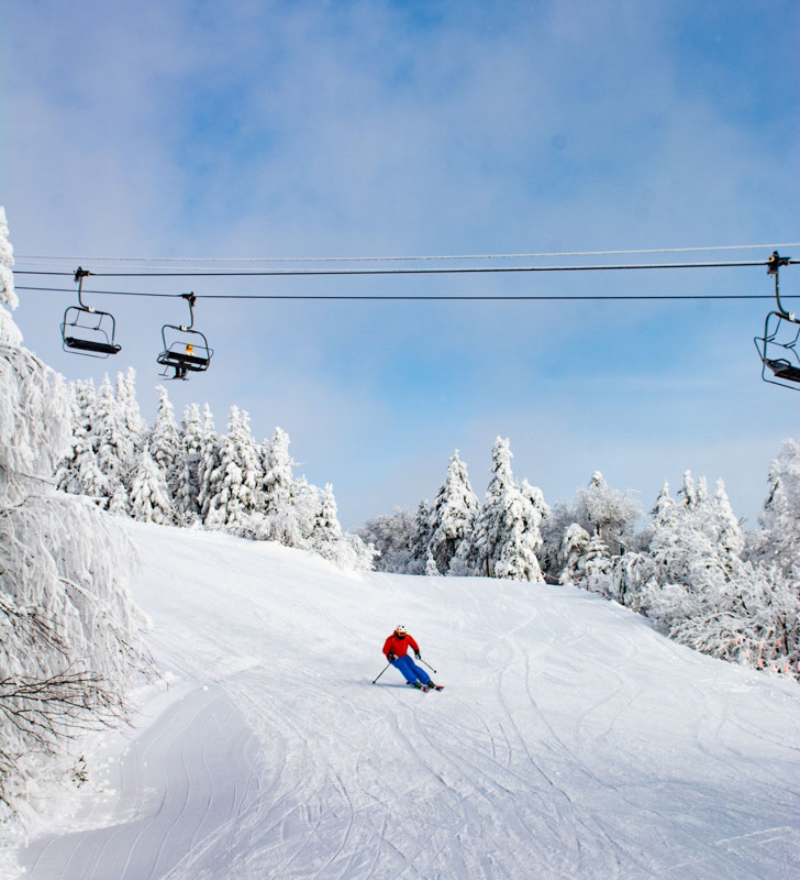 Skier in red jacket and blue pants skis down a run