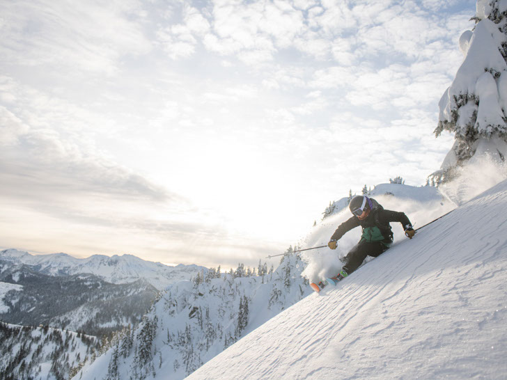 Skier carving a turn on a run with snow spraying behind them in Stevens Pass