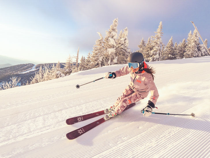 Skier in pink outfit smiles as she carves a turn on a groomed run