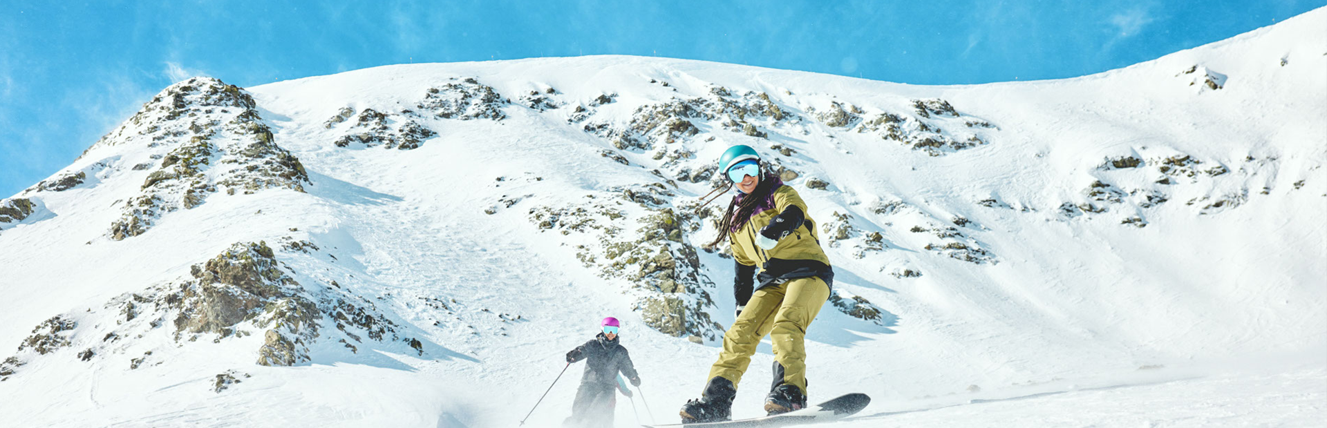 Girl snowboarding in front of a person skiing on snowy mountain