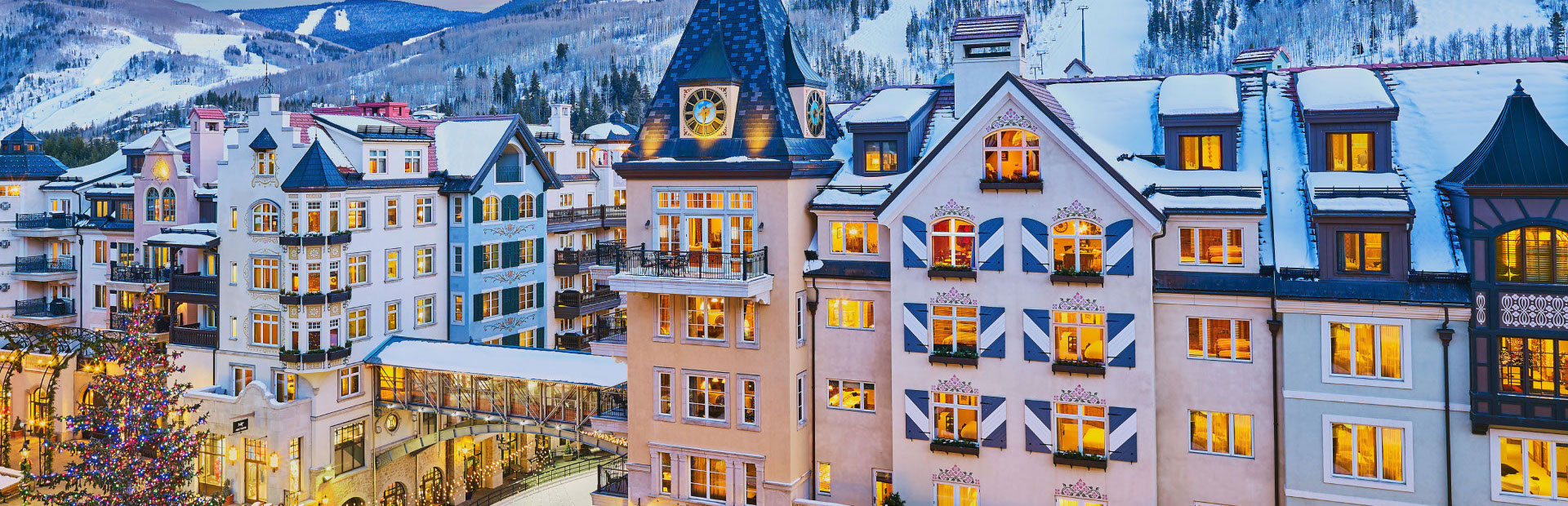Vail Village buildings lit up at dusk with snowy mountains in the background