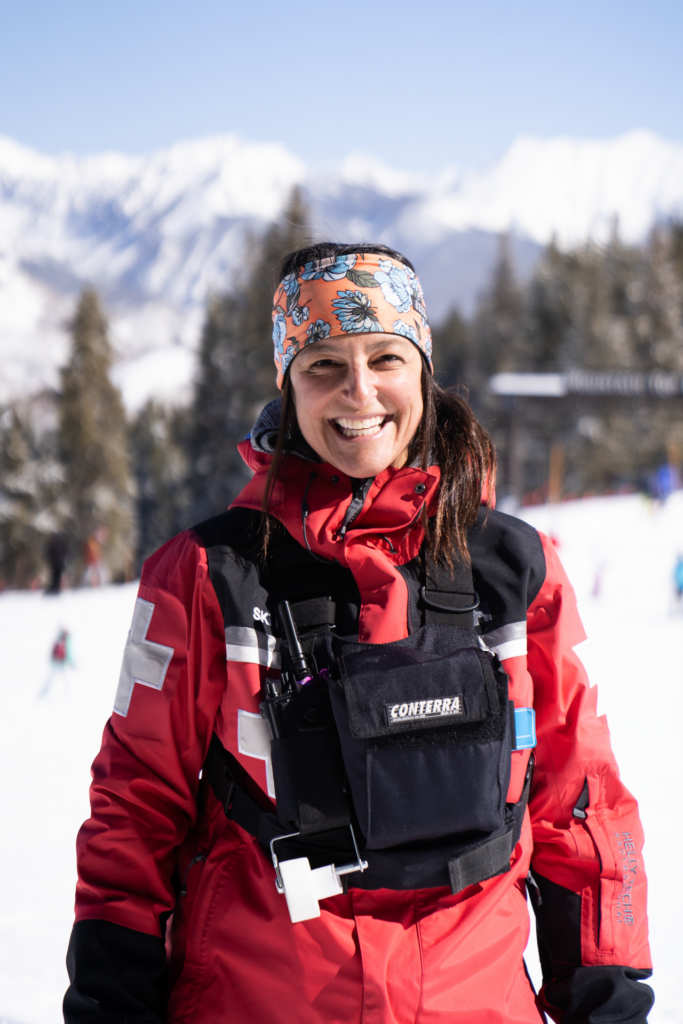 Woman in red ski patrol jacket standing and smiling on snowy ski slope