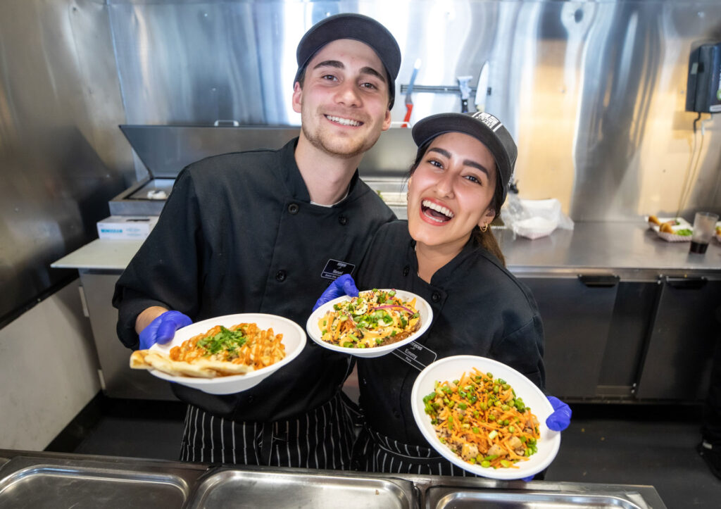 Image of two front line employees smiling while working in a kitchen 