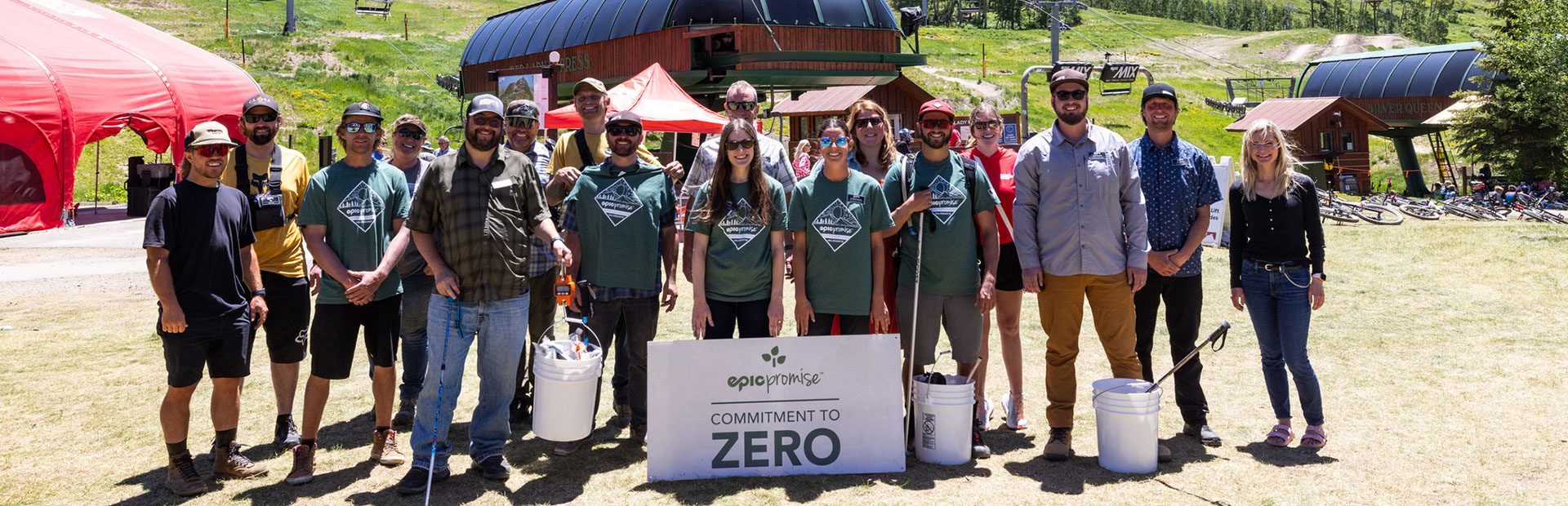 Vail employees standing with buckets and poles to clean up trash at the base of a ski lift in the summer