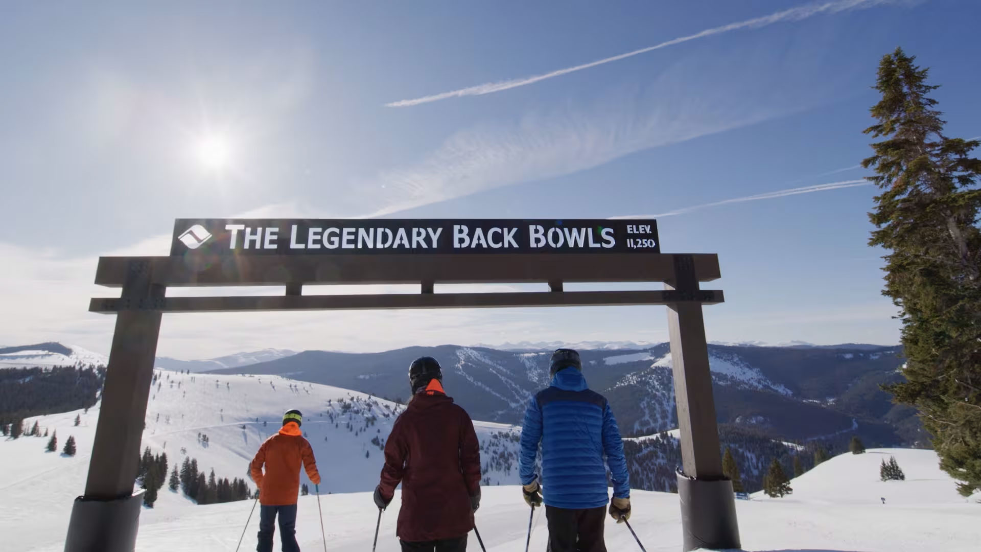 3 skiers entering Vail's back bowls under a sign that reads The Legendary Back Bowls Elev. 11,250