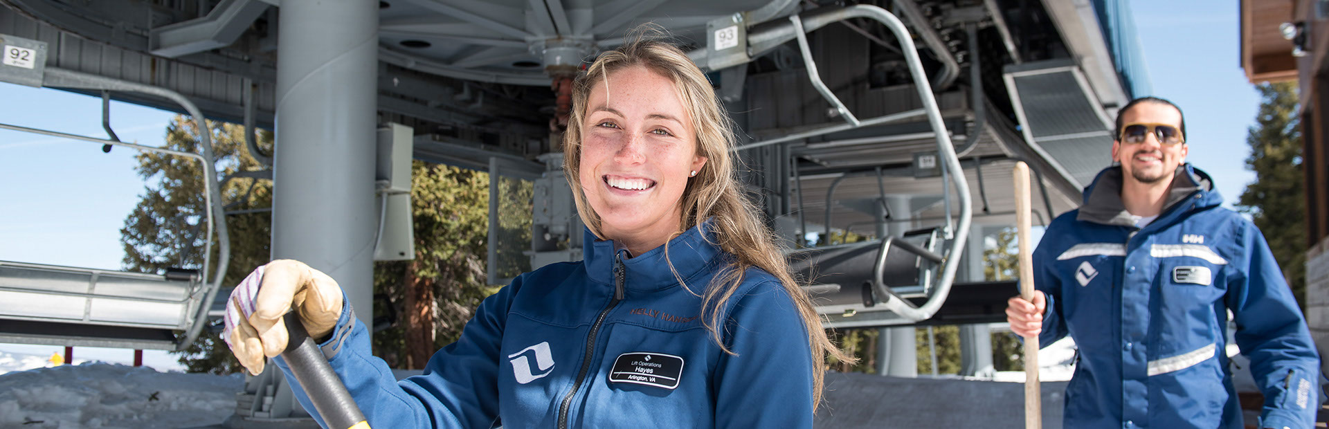 Two Vail resorts employees smiling and standing in front of a chair lift.