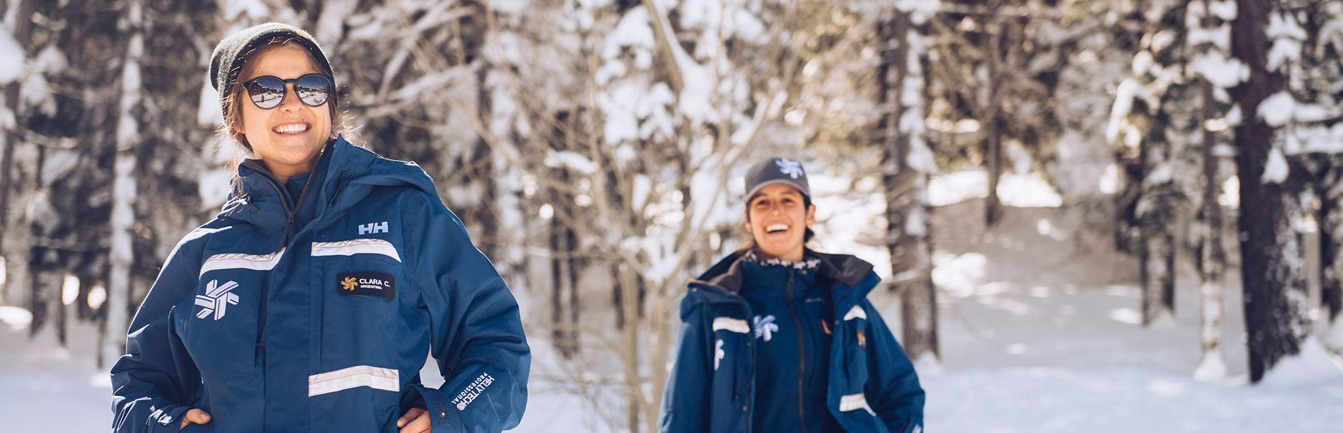 Two employees wearing ski jackets smiling with snowy trees in the background
