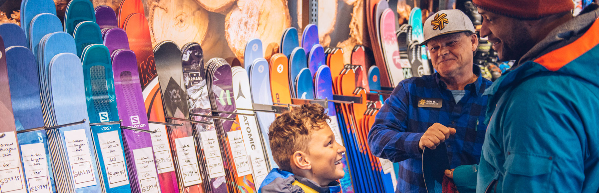 Man and child looking at snowboard with a ski shop employee with skis in the background