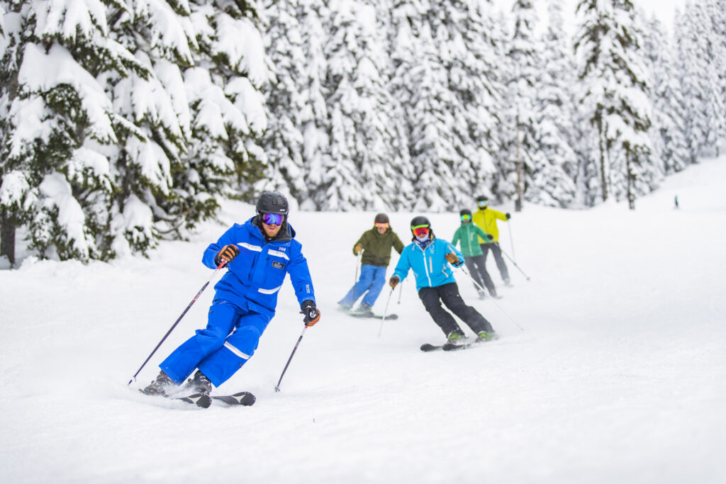 Ski instructor leads group of adults down a groomed ski hill in Stevens Pass