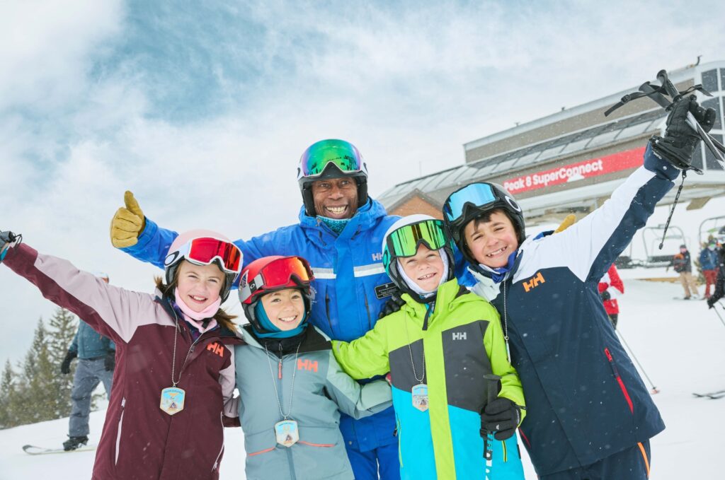 Ski school instructor posing with kids with their arms up in excitement