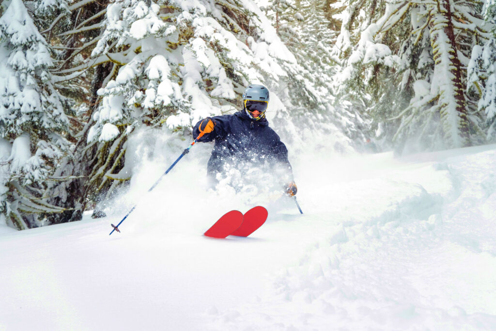 Skier in a blue coat wearing a helmet skiing through powder