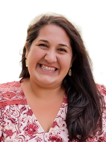 Woman with brown hair smiling while wearing a red patterned shirt