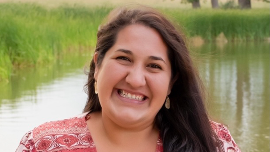 Woman with brown hair smiling while wearing a red patterned shirt