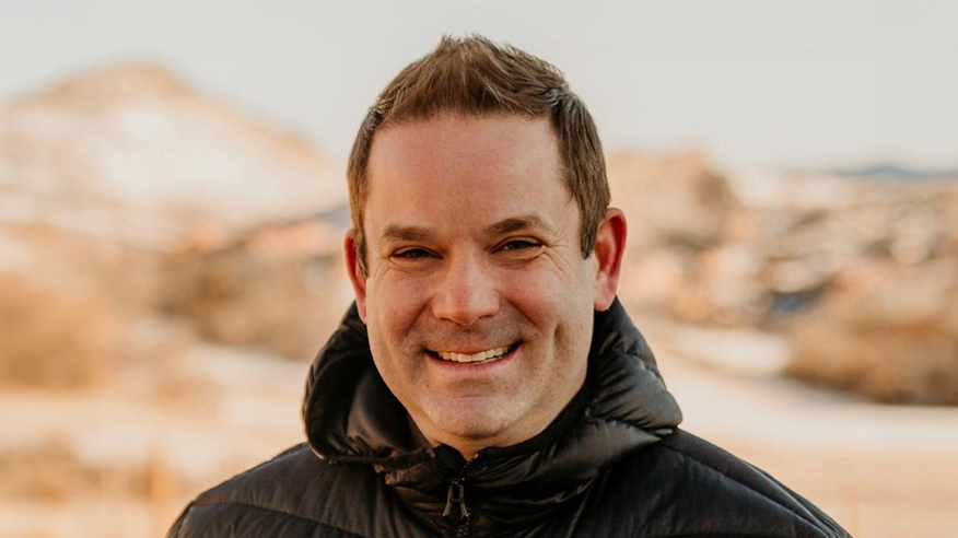 A man with short brown hair wearing a puffy black coat and smiling