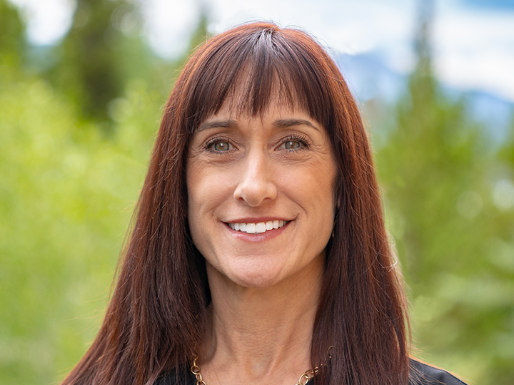 Woman with red-ish brown hair and bangs smiling